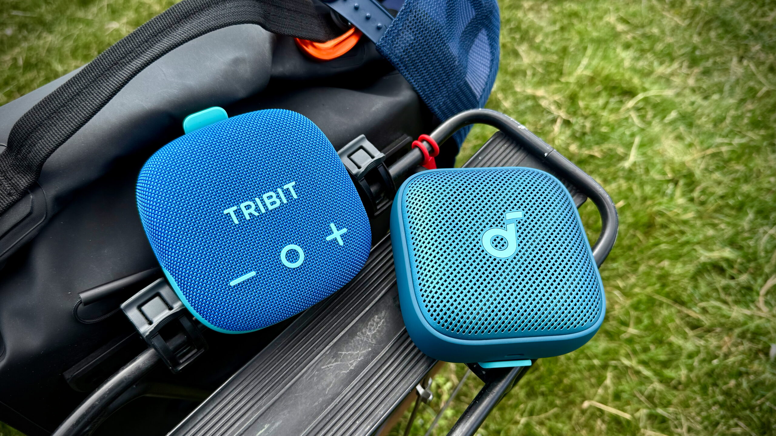 Bose SoundLink Micro (2nd Gen) alternatives - 2 (2) The Tribit StormBox Micro 3 and Soundcore Boom Go 3i attached to a bicycle rear rack beside a bike bag.