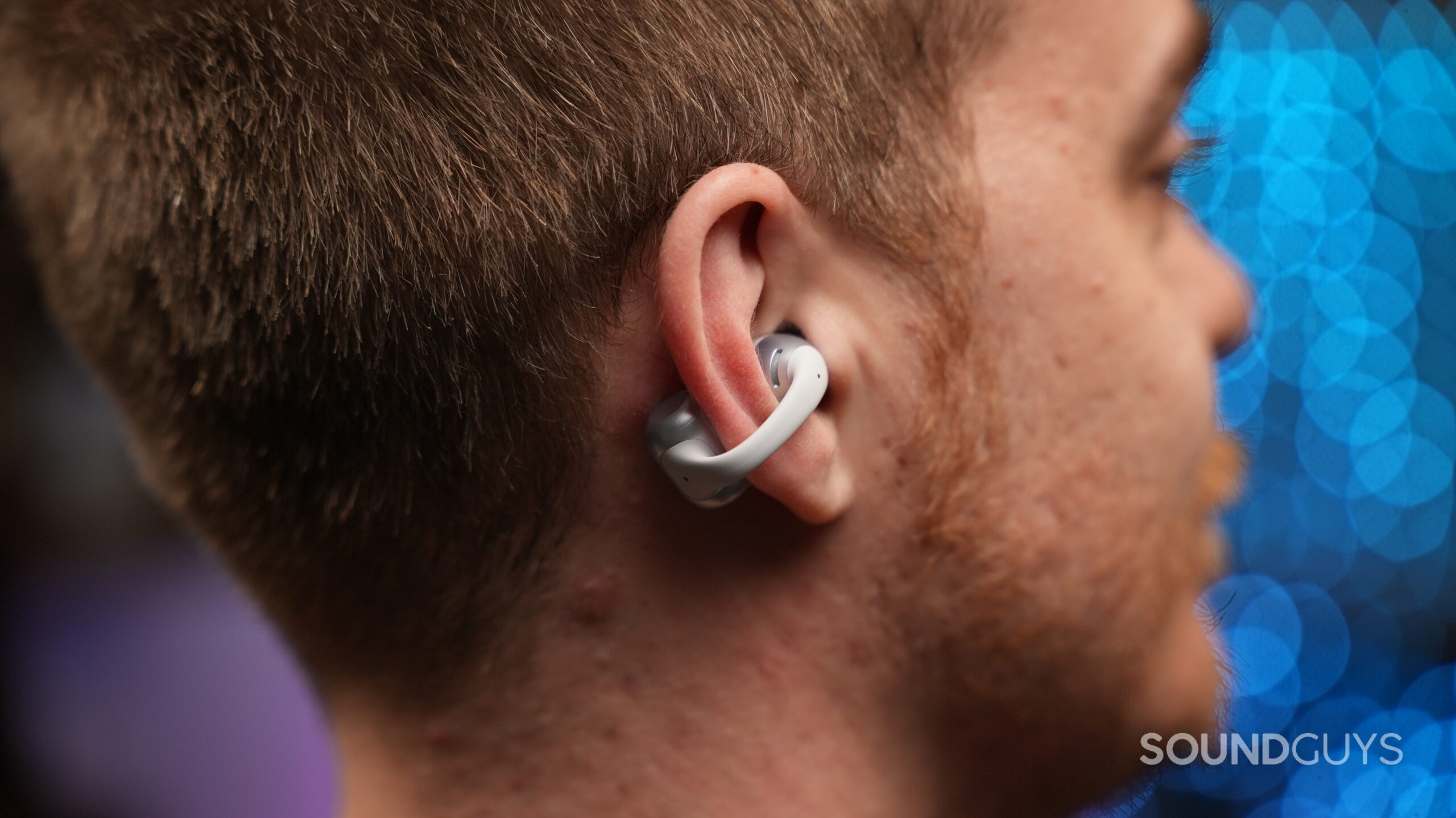 A person wears the Shokz OpenDots ONE open-ear earbud. The clip-on design wraps around the outer ear, with the speaker positioned near the ear canal and the battery module resting behind the ear.