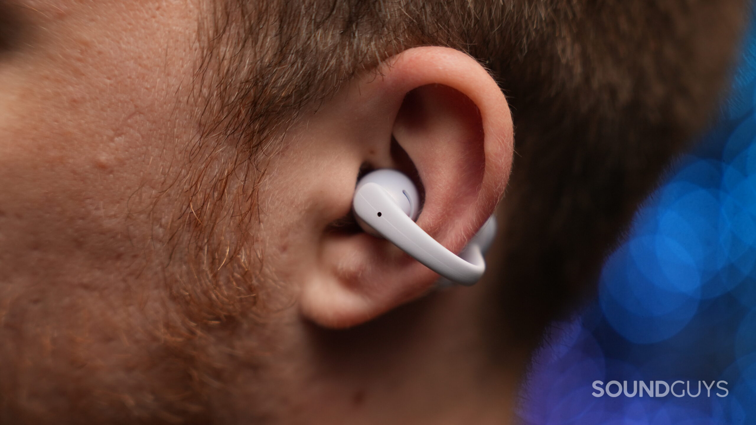 Close-up side view of a person wearing the Shokz OpenDots Air. The lightweight clip-on earbud hooks around the ear, leaving the ear canal unobstructed while positioning the speaker just outside the ear.