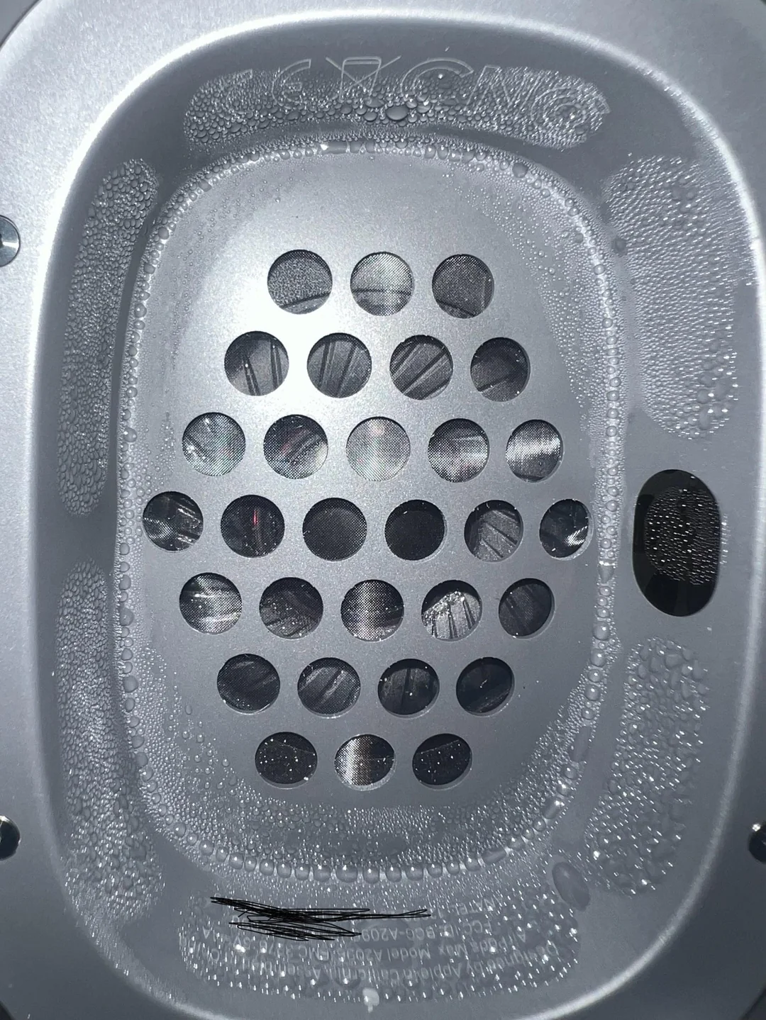 Macro photo of an Apple AirPods Max ear cup covered in heavy condensation, with water droplets coating the aluminum interior and collecting around the speaker grille after extended use.