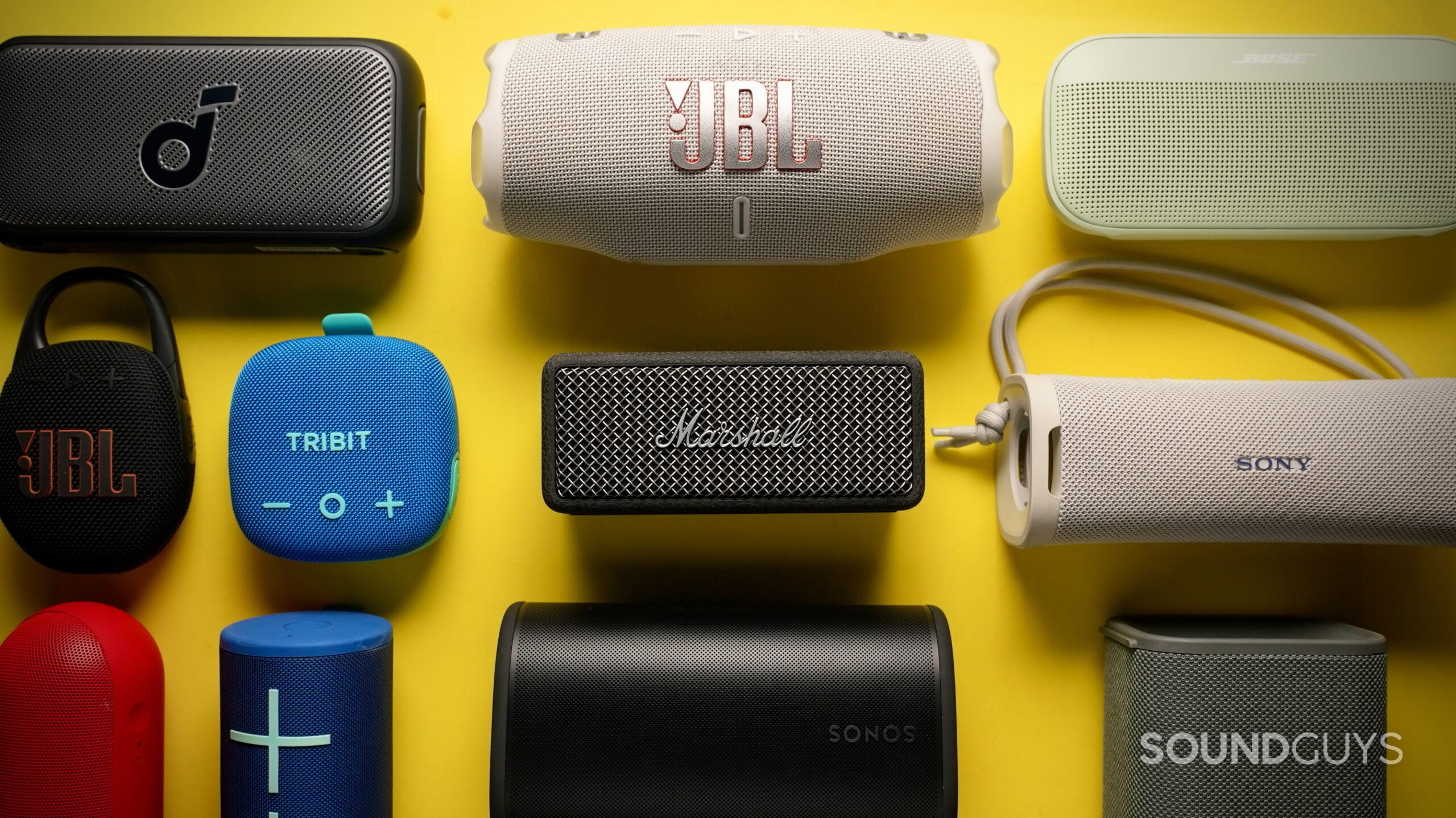 Top down photo of many different sized Bluetooth speakers on a yellow background.