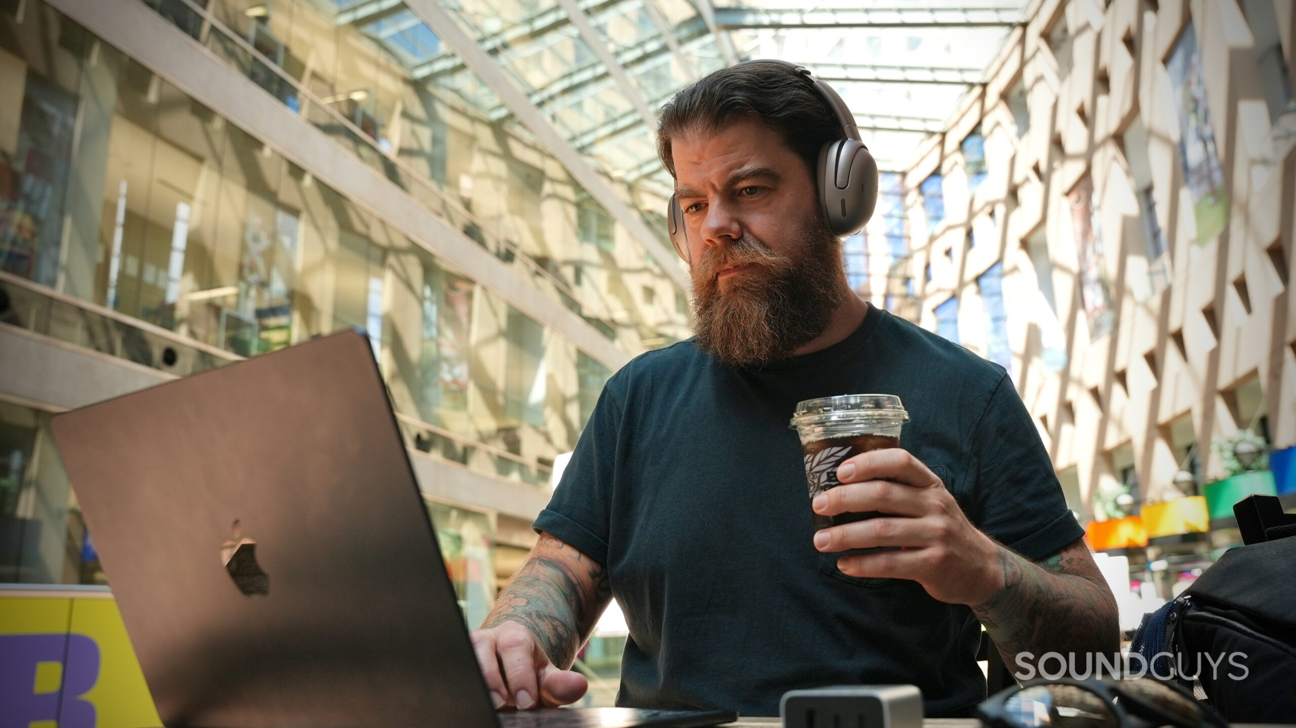 JBL Tour One and AirPods Pro 3 Travel feature - 1 A person wearing the JBL Tour One M3 headphones while working on a laptop with a coffee nearby.
