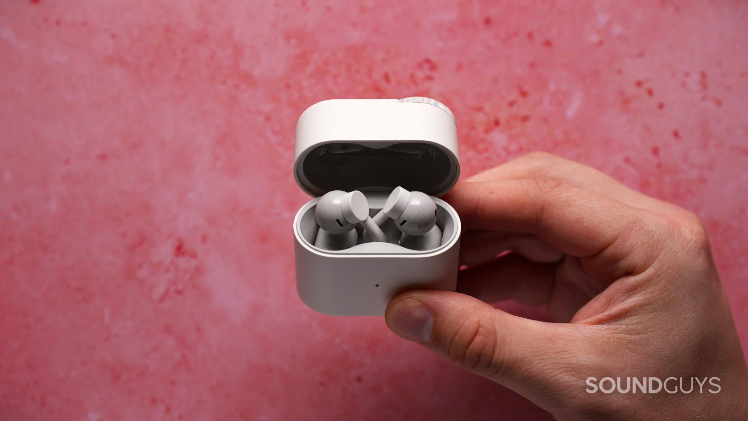 A hand holds the open CMF Clip Pro charging case with the white clip-on earbuds inside against a pink background.