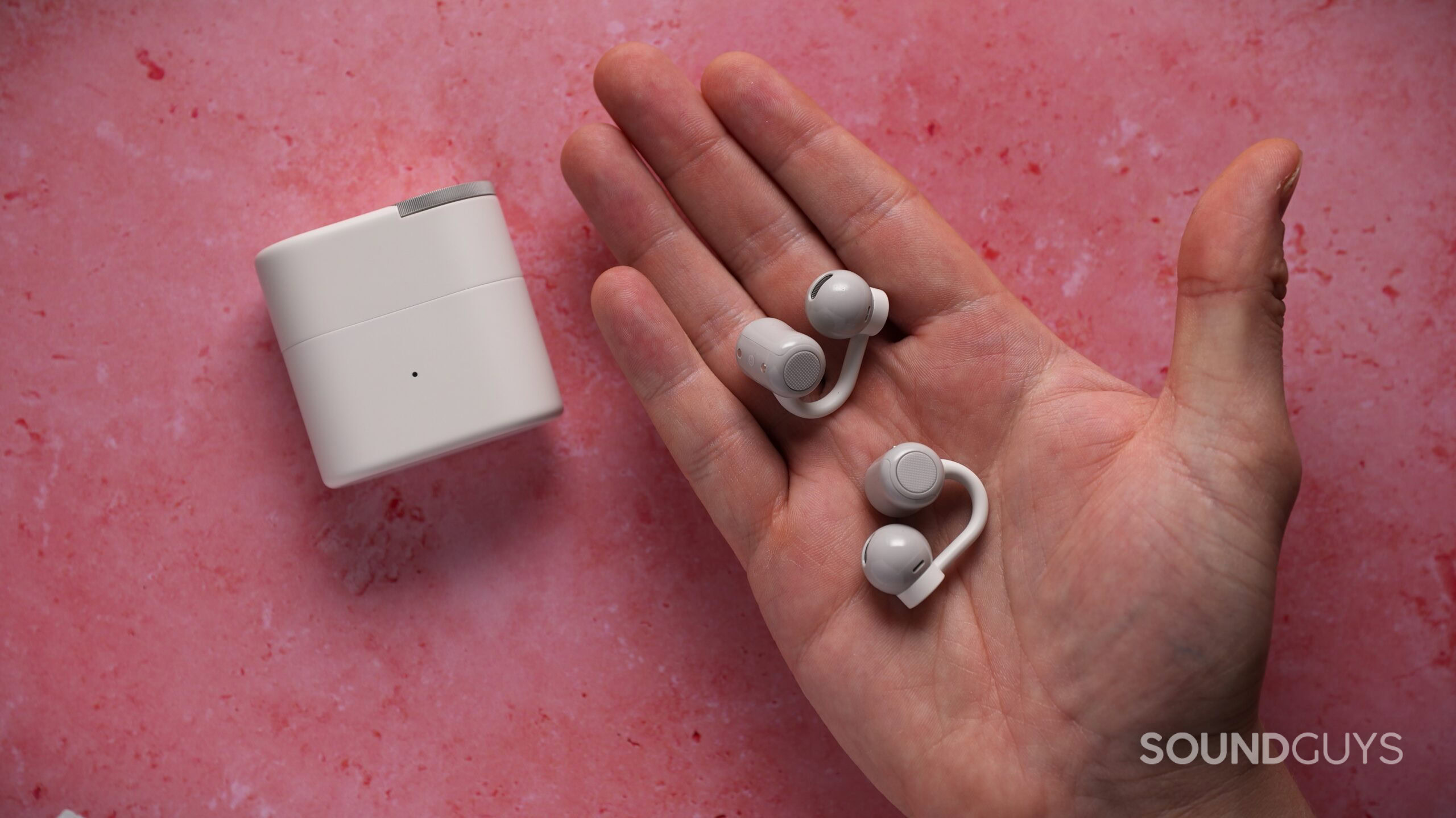 A pair of white CMF Clip Pro earbuds rests in a person’s palm beside the matching charging case.
