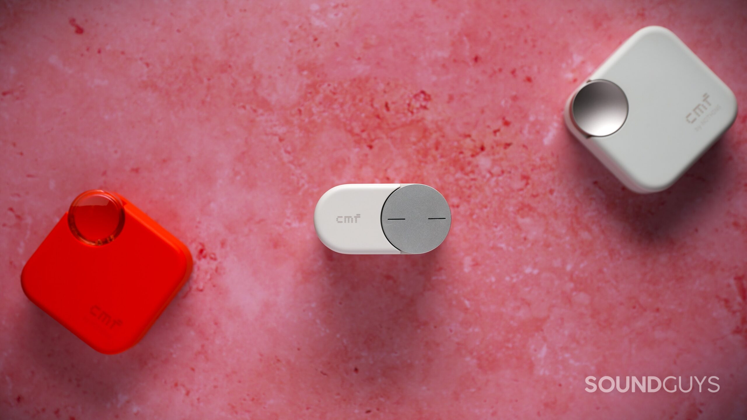CMF Clip Pro The white CMF Clip Pro case displayed between red and white CMF earbud charging cases on a pink background.