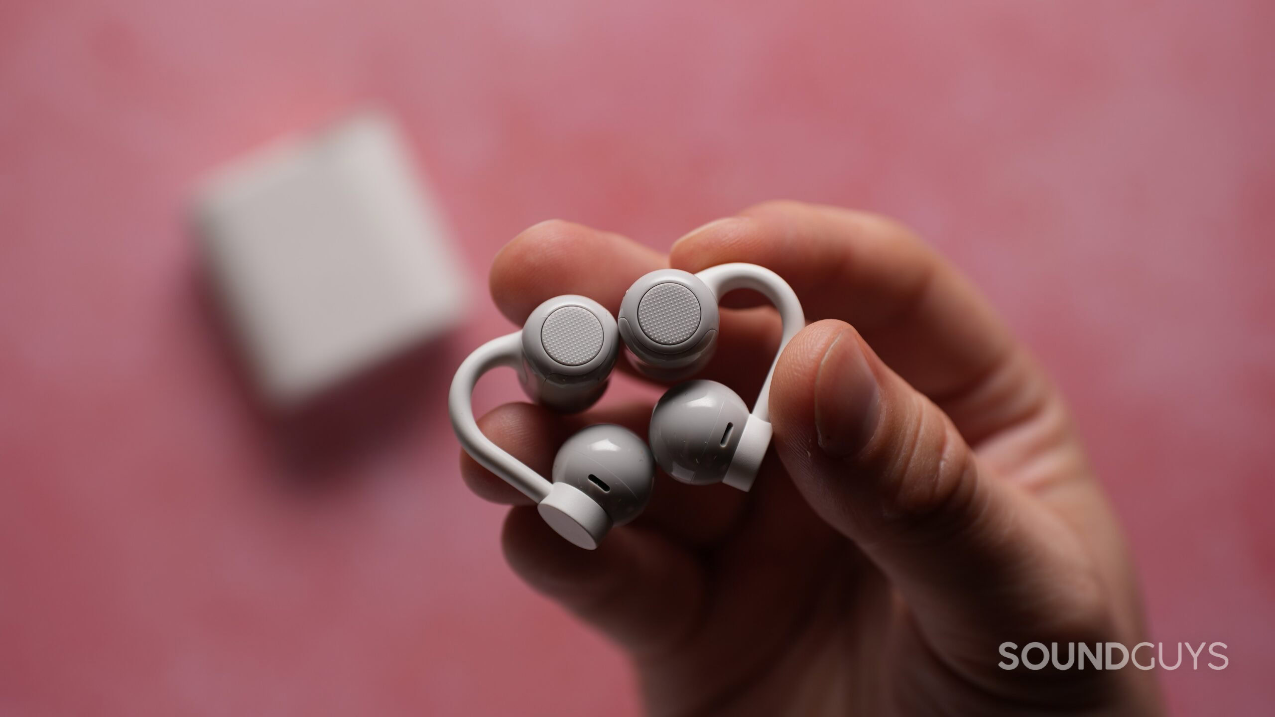 Close-up of the CMF Clip Pro earbuds held in one hand, showing their circular touch-control surfaces and flexible ear clips.