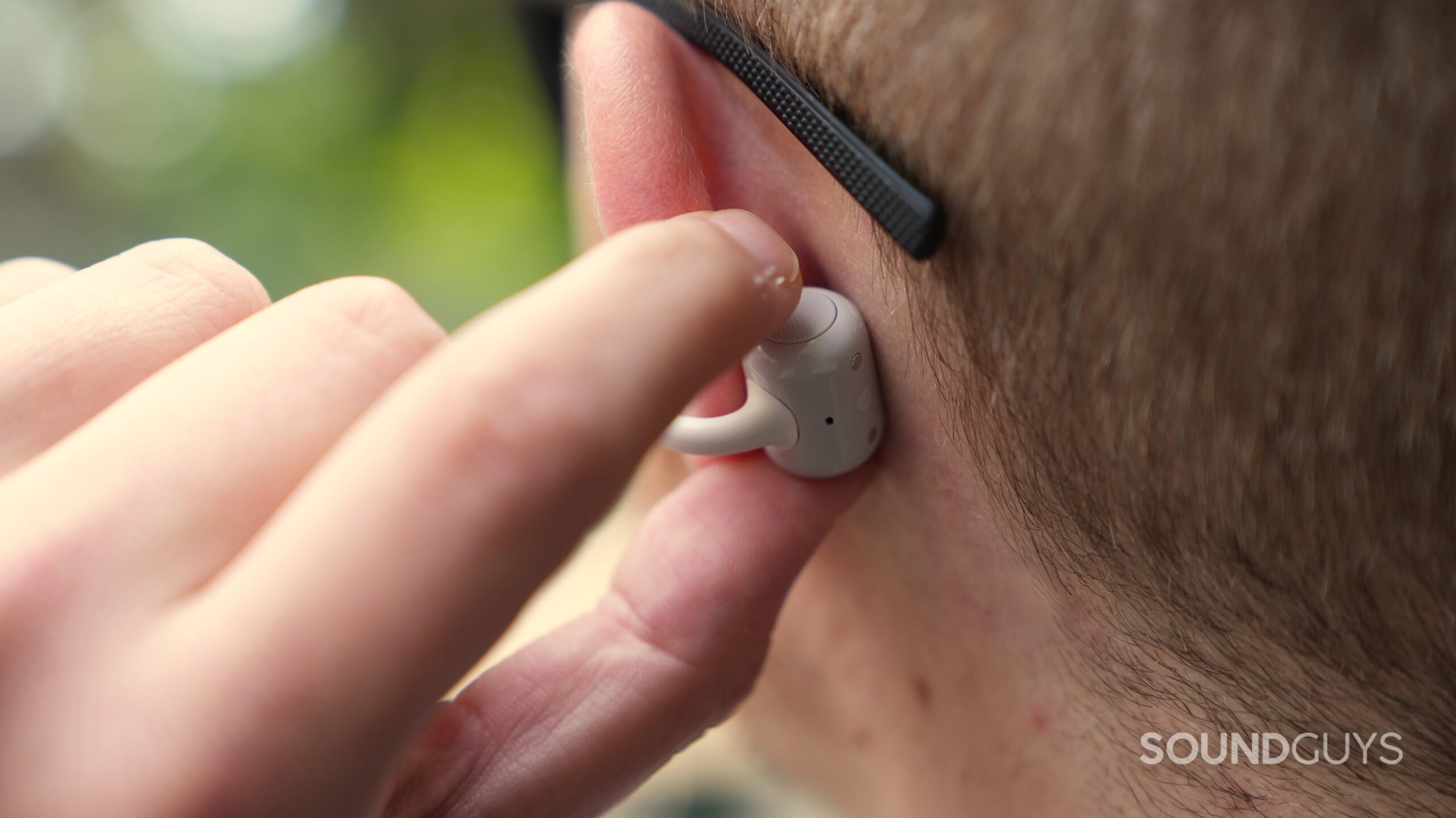A man presses the circular control on a CMF Clip Pro earbud while wearing it.