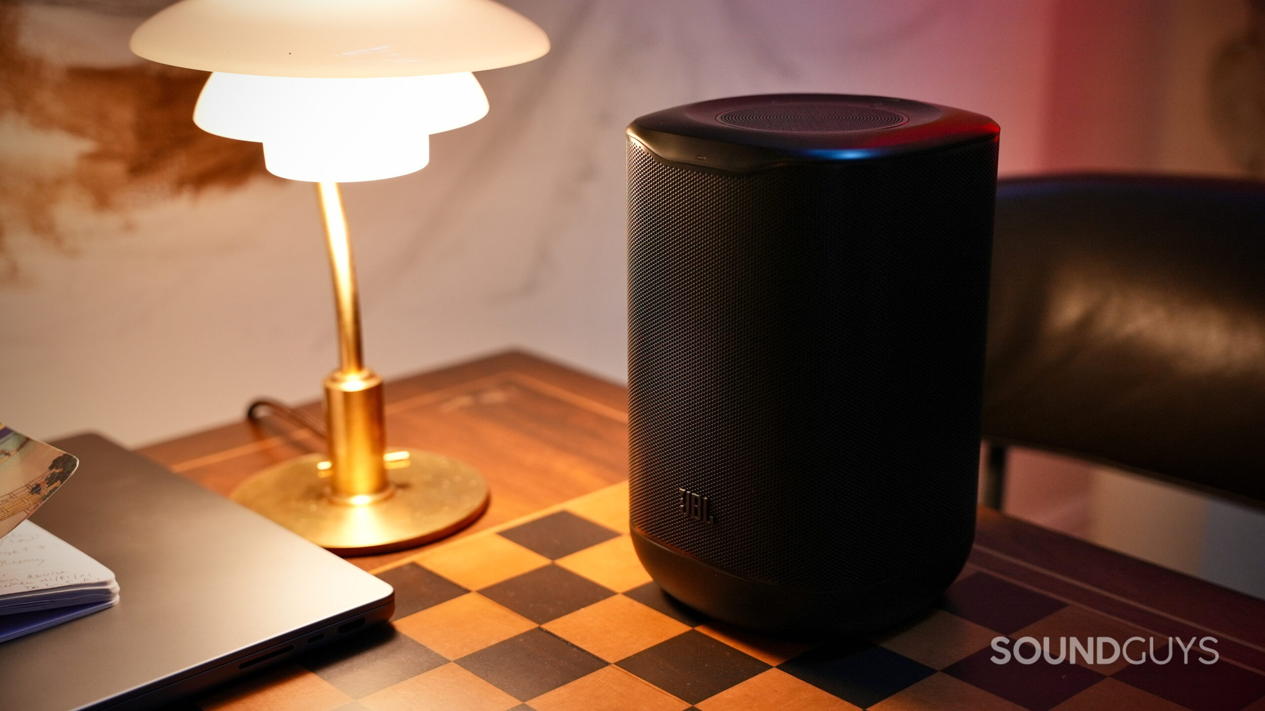 JBL Cove Series - 8 Black JBL Cove P1 Wi-Fi speaker sitting on a table next to a lamp and laptop.