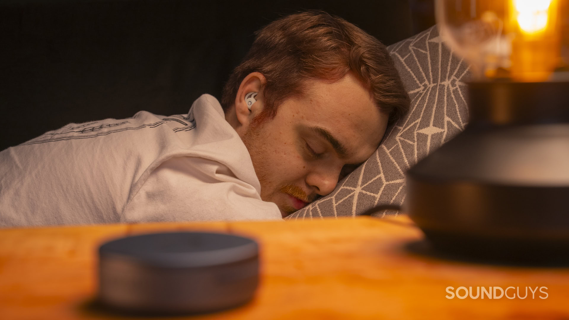 SG_Ozlo Sleepbuds 2-4 Person sleeping on their side while wearing Ozlo Sleepbuds 2, with the charging case on the bedside table.