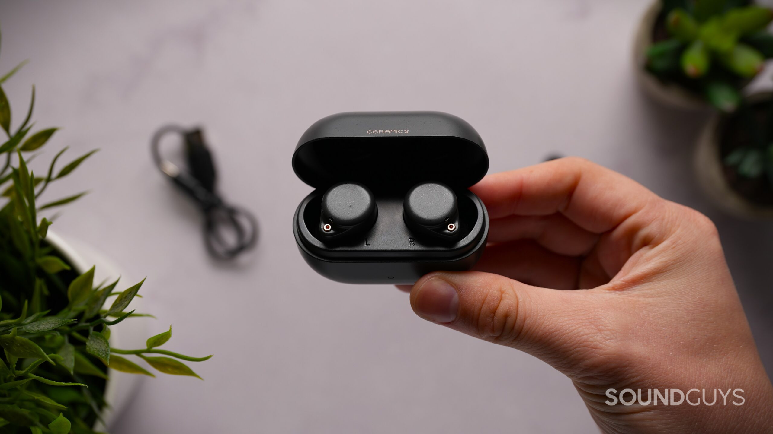 A hand holds the open charging case containing the black ROSESELSA Ceramics Ultra earbuds.