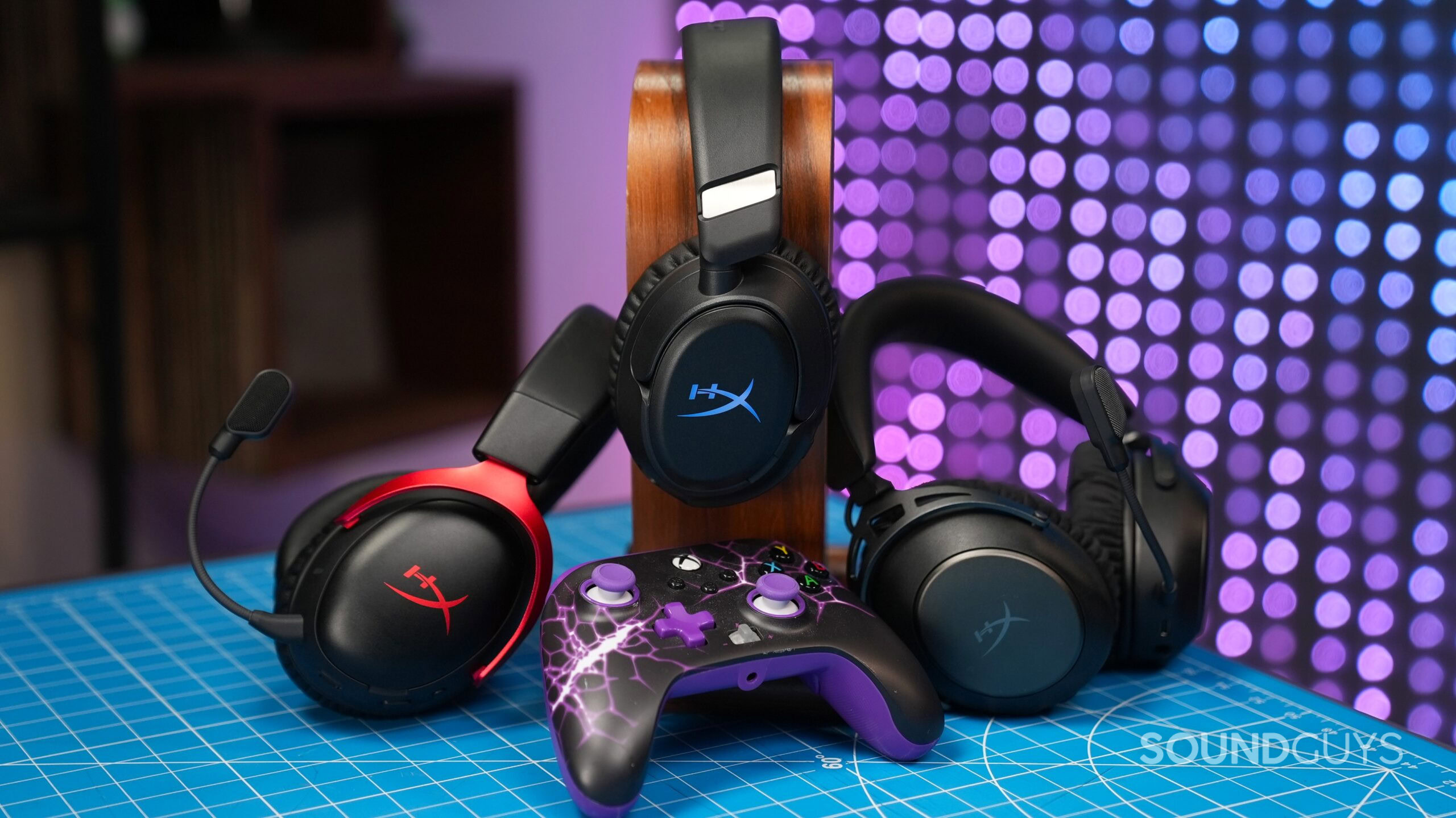 hyperx gaming headsets hero Three HyperX gaming headsets displayed around a wooden stand with a purple Xbox controller in front.