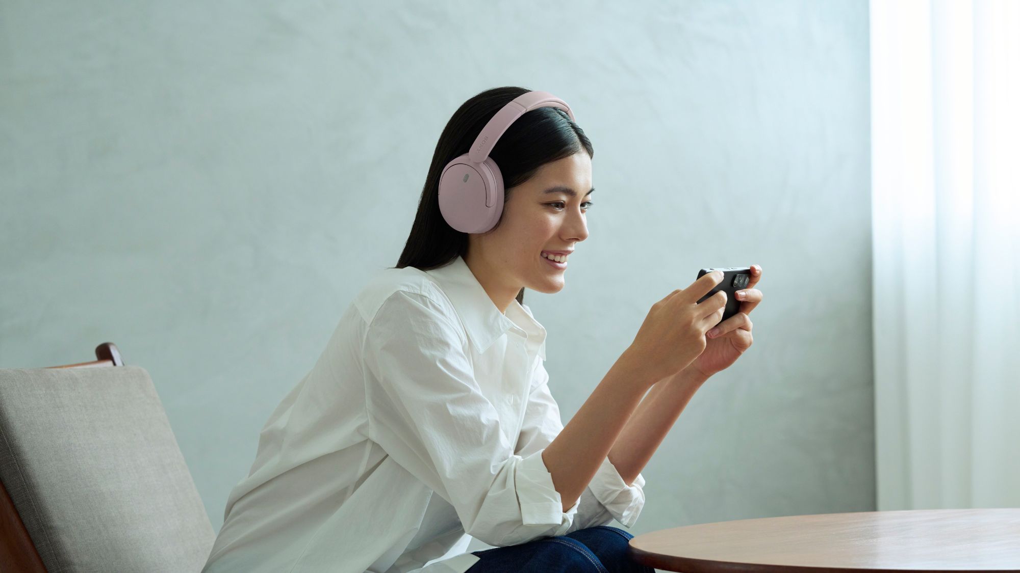 A woman playing games with the Sony WH-CH730N headphones over her ears