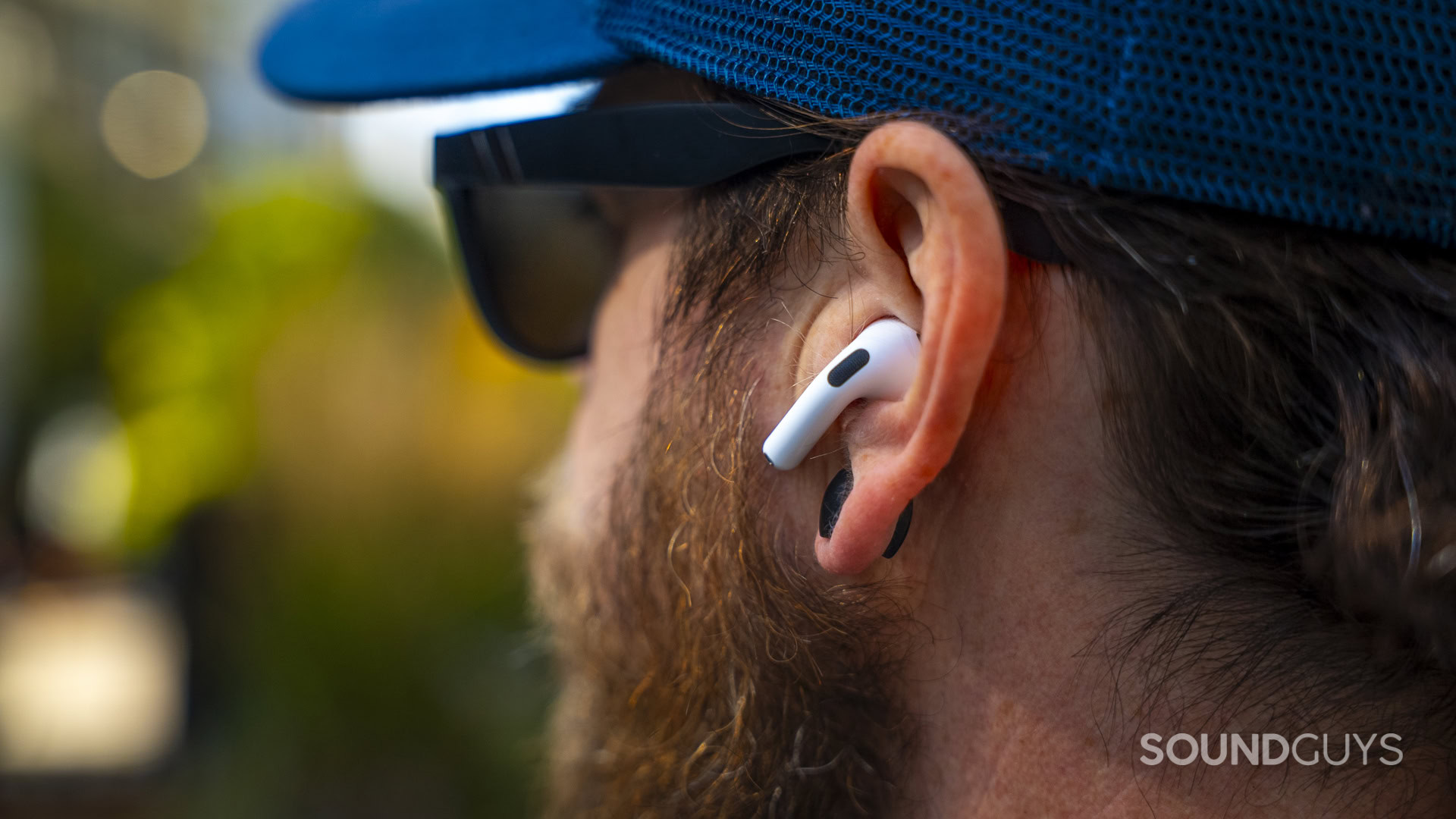 Close-up of a white Apple AirPod resting in a man’s ear.