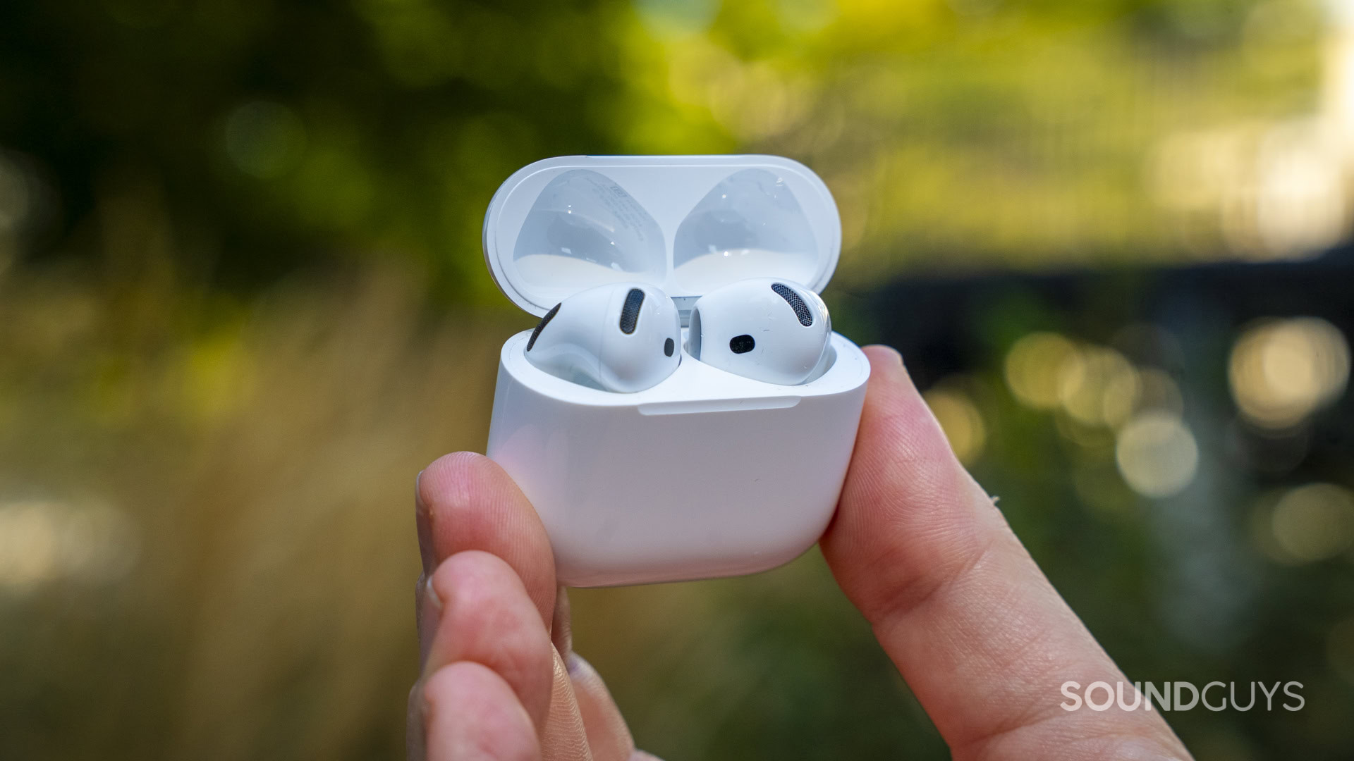 White Apple AirPods inside an open charging case held outdoors.