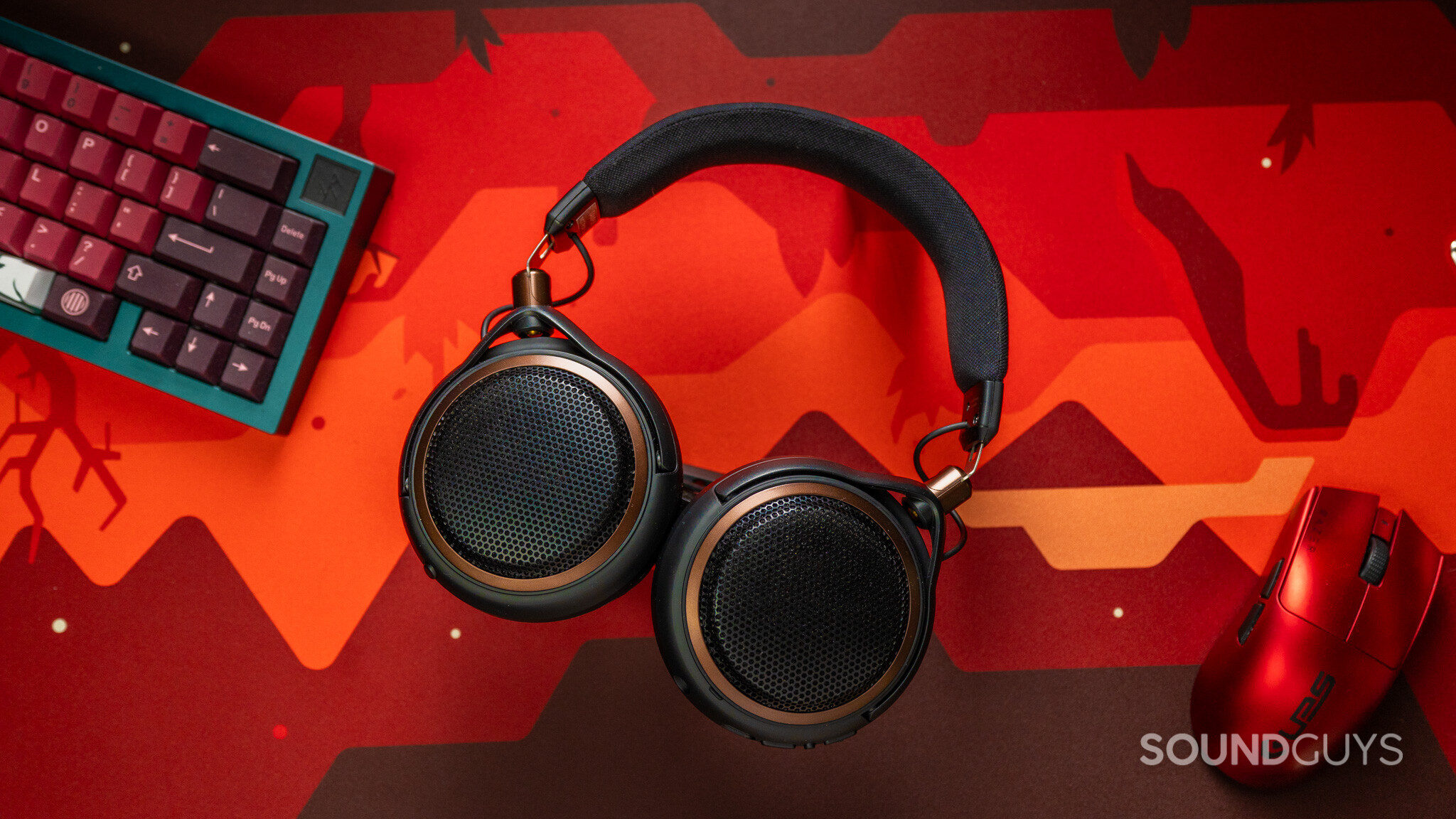 ATH-AL5NC Top down with red background Audio-Technica ATH-AL5NC headphones with black mesh earcups and bronze trim on a red patterned desk mat between a keyboard and mouse.