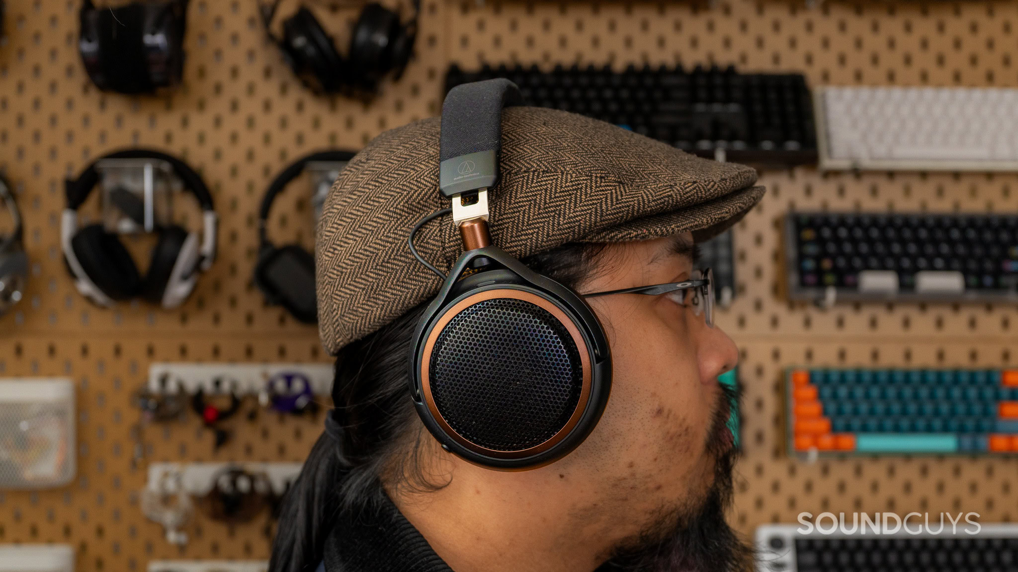 ATH-AL5NC Worn Side view of a person wearing Audio-Technica ATH-AL5NC headphones over a brown flat cap, with glasses and a headphone display behind them.