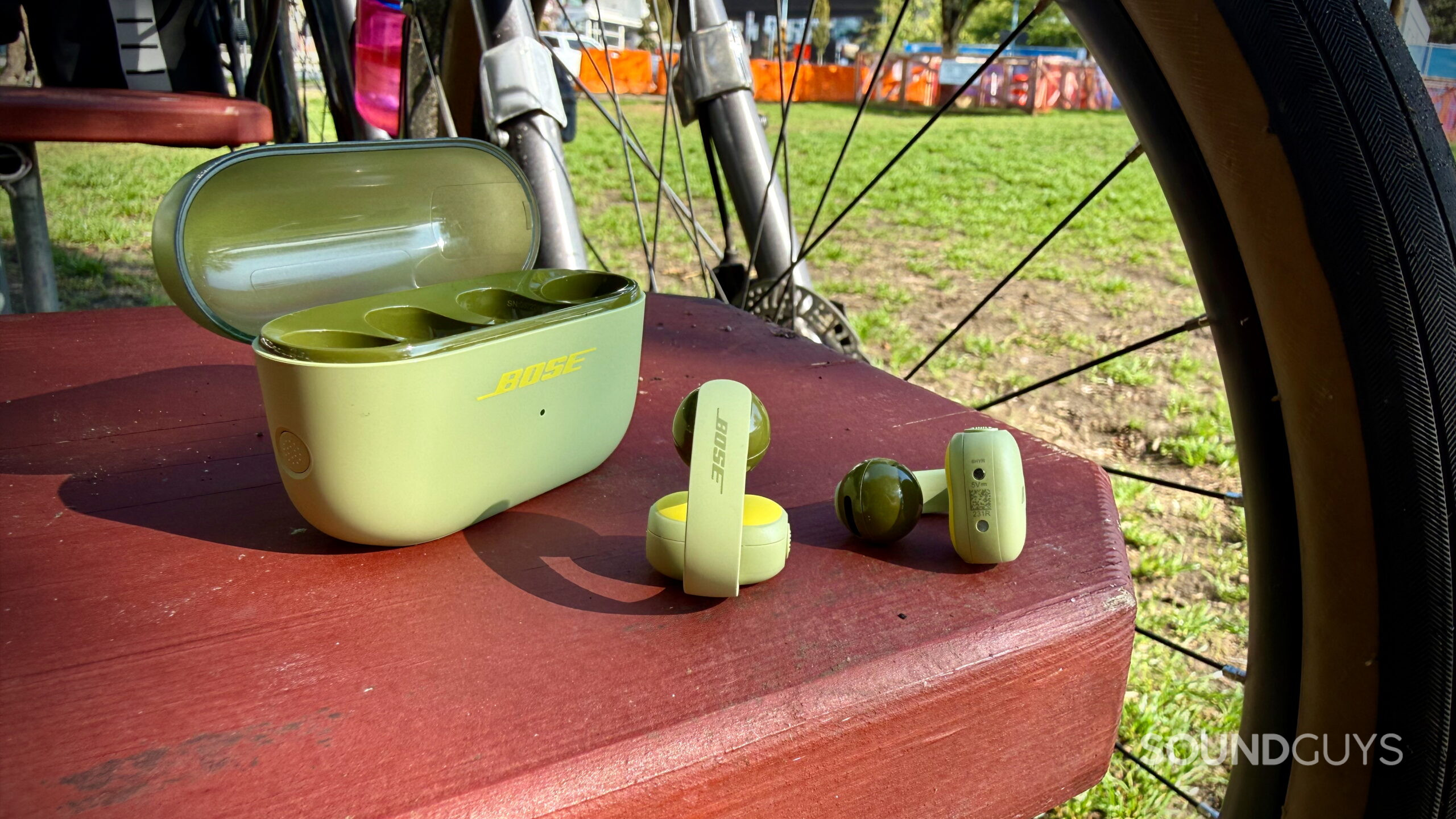 Bose Sport Open Earbuds - 3 (1) Bose Sport Open Earbuds and charging case beside a bicycle.