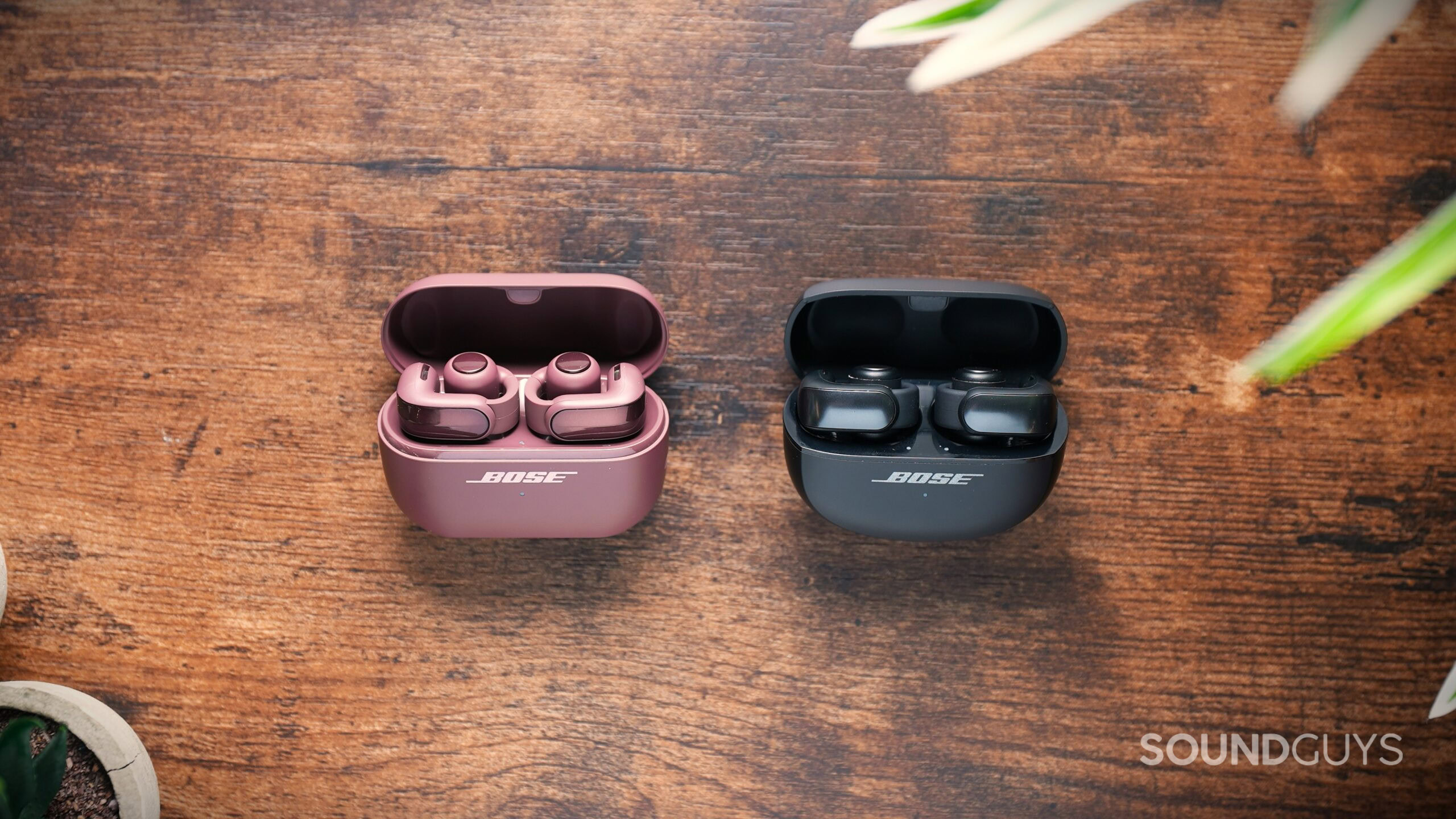 Bose Ultra Open 1 vs 2 Cherry Chocolate Bose Ultra Open 2 earbuds on the left beside the original black Bose Ultra Open earbuds, both in open charging cases.