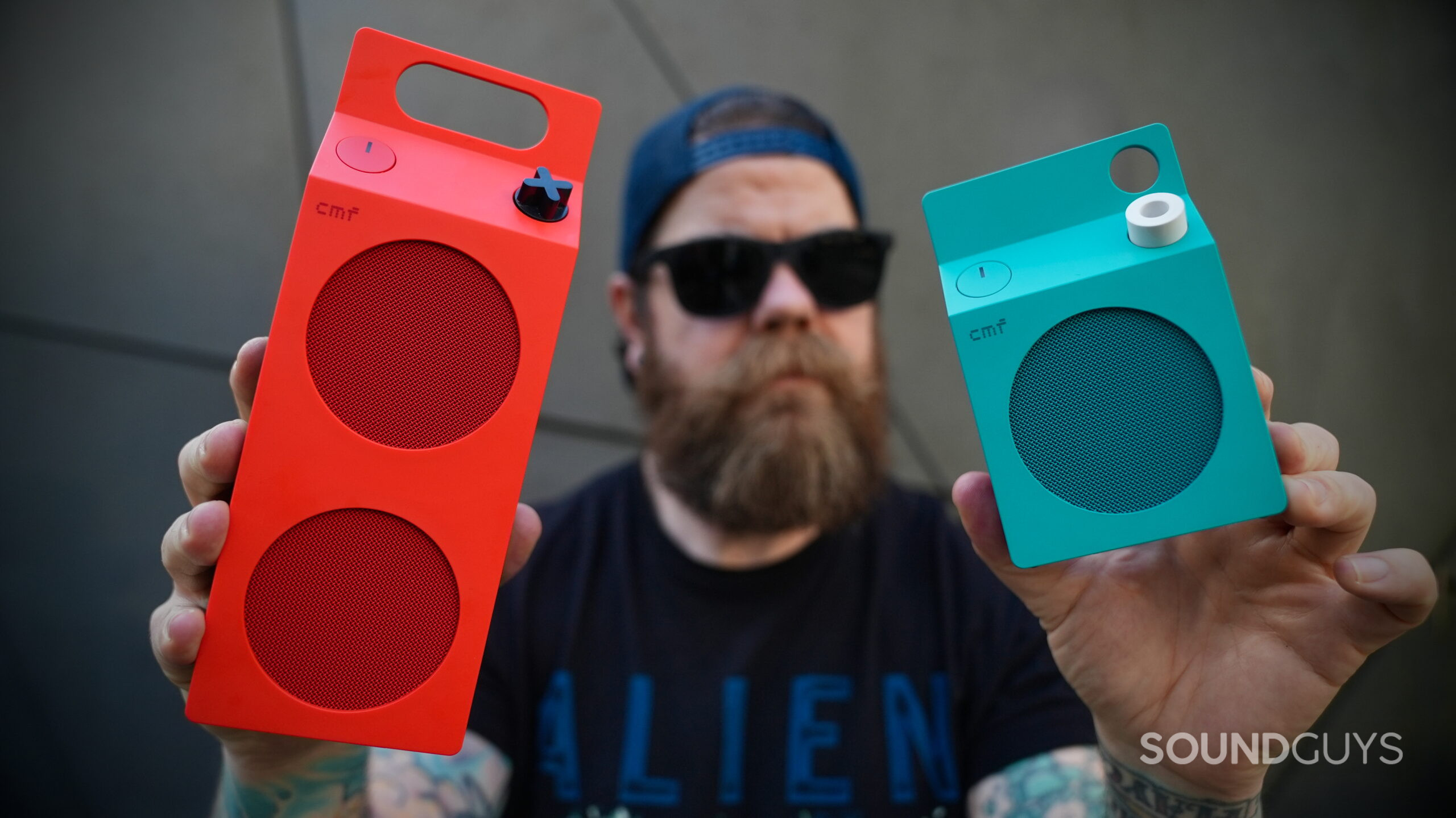 CMF Speaker S and M Edits - 1 Orange CMF Speaker M and turquoise Speaker S held toward the camera, showing their front grilles and control knobs.