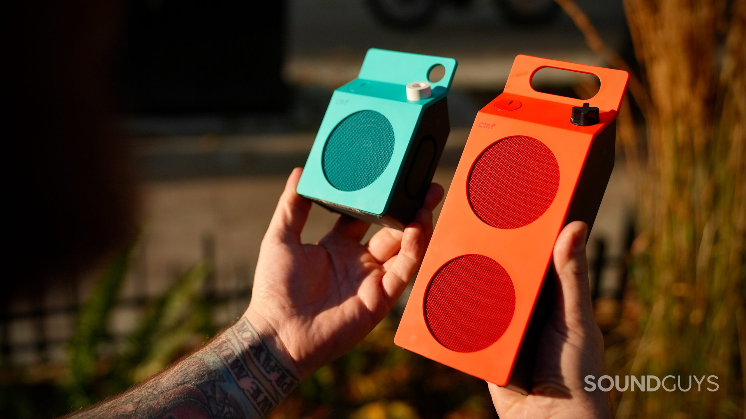 CMF Speaker S and M Edits - 2 Person holding the turquoise CMF Speaker S and orange Speaker M side by side outdoors.