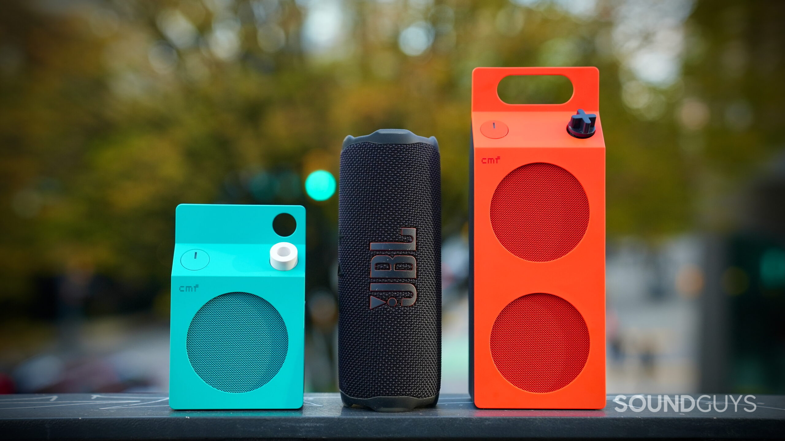CMF Speaker S and M Edits - 8 CMF Speaker S in turquoise and Speaker M in orange standing beside a black JBL portable Bluetooth speaker.