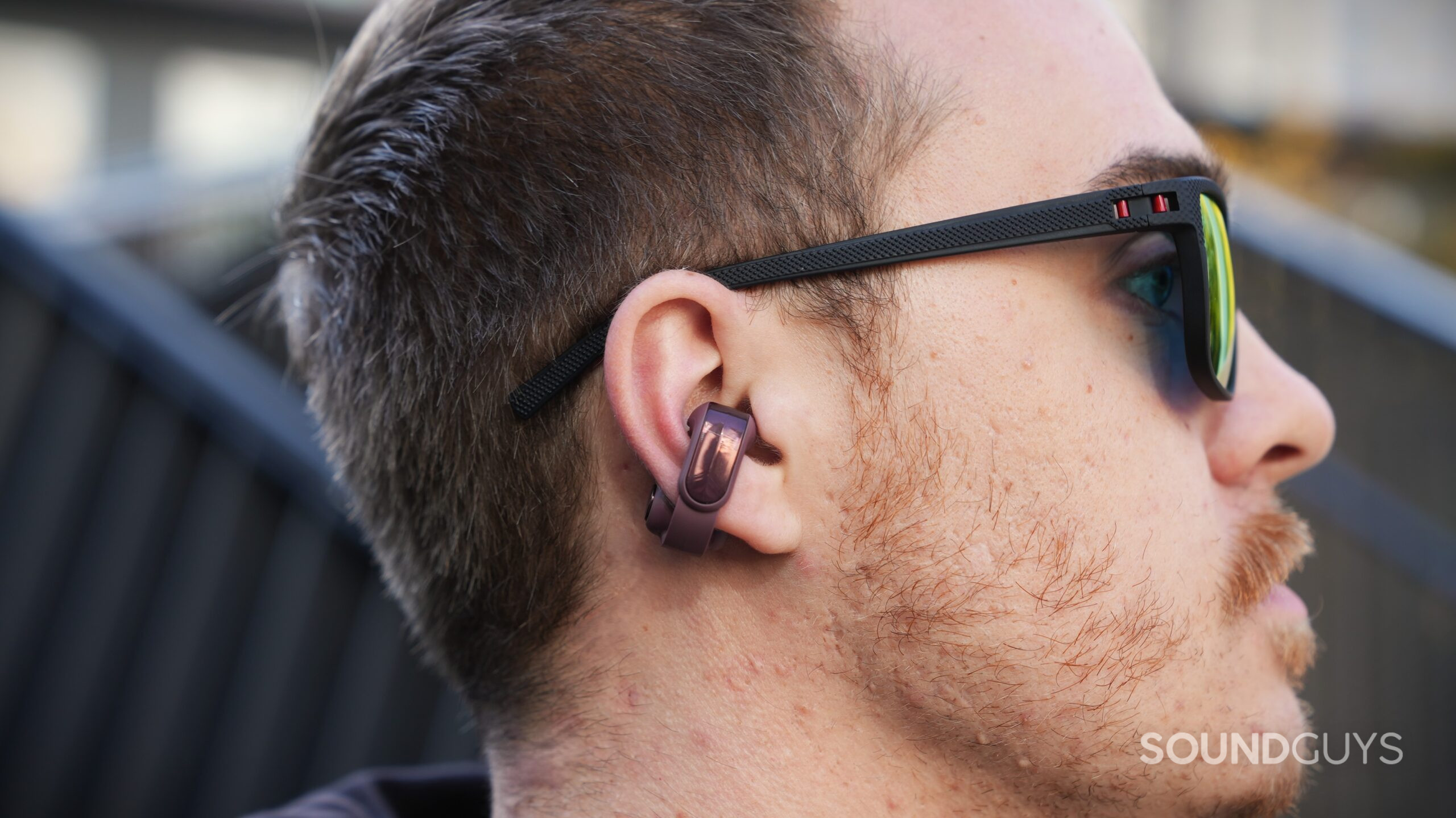 DSC09914 Side profile of a person wearing sunglasses and a Cherry Chocolate Bose Ultra Open 2 earbud clipped around the lower ear.