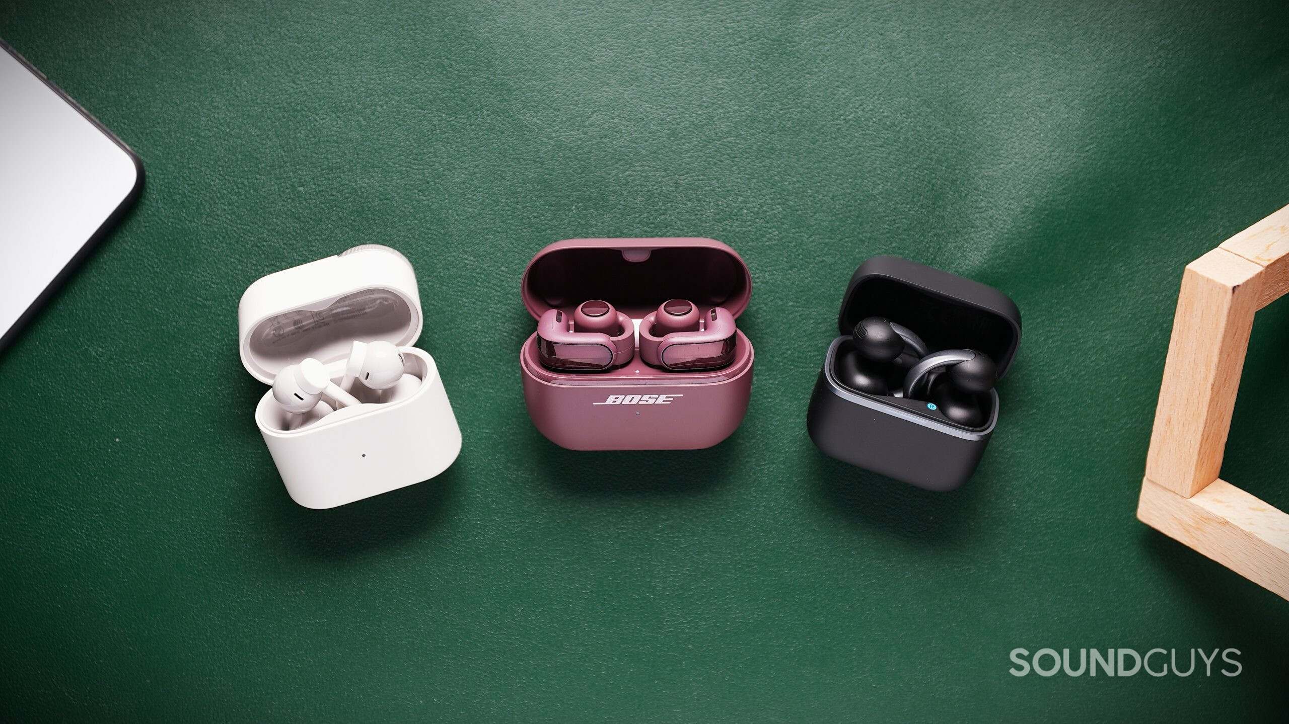 DSC09976 Three pairs of earbuds in open charging cases on a green surface, with cherry chocolate Bose earbuds between white and black pairs.
