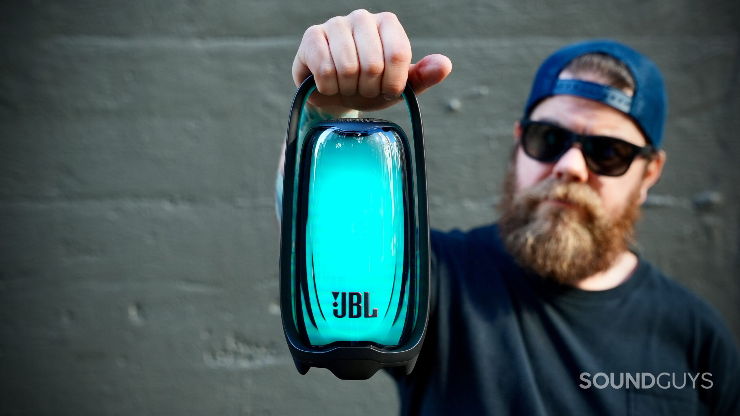 JBL Pulse 6 glowing blue-green while being held by its integrated handle.