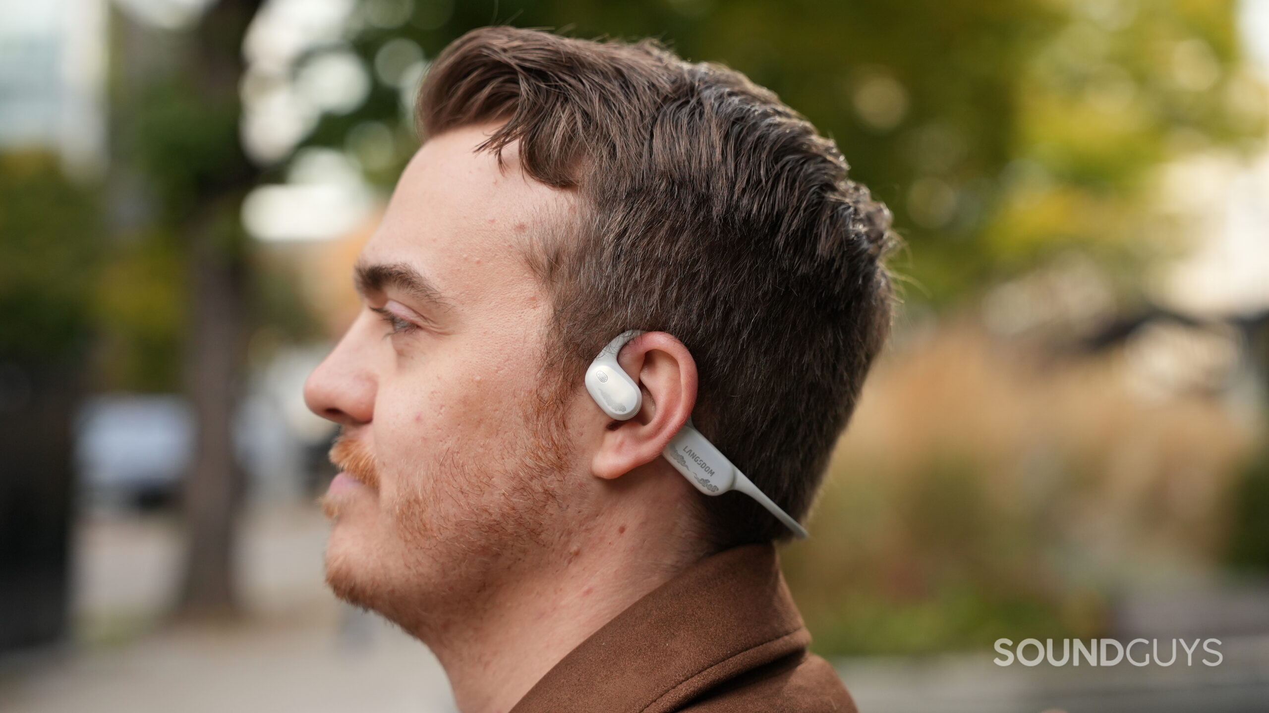 listening to airwave pro 2 Side profile of a person wearing the Langsdom AirWave Pro 2 open-ear headphones outdoors.